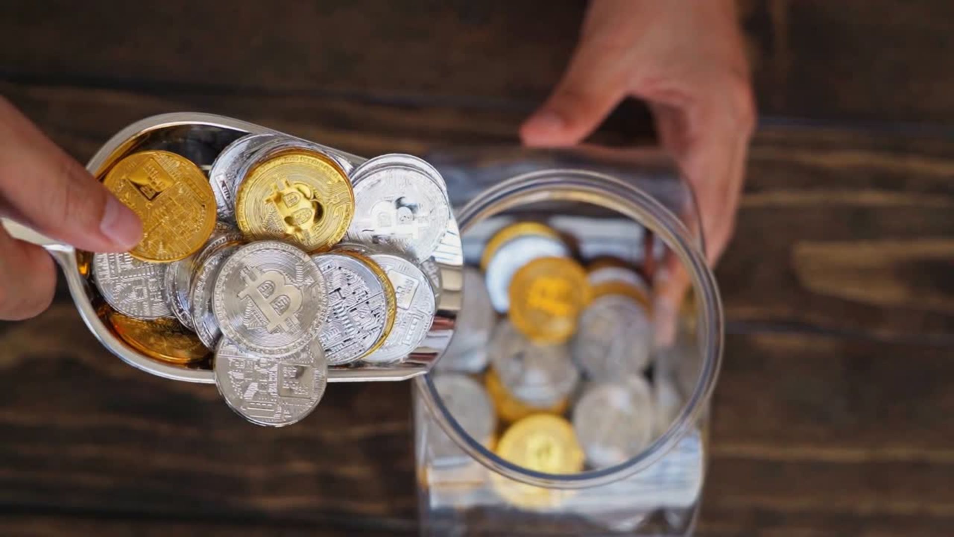 Mano vertiendo criptomonedas físicas de Bitcoin doradas y plateadas en un tarro, símbolo de los airdrops como reparto gratuito de tokens.